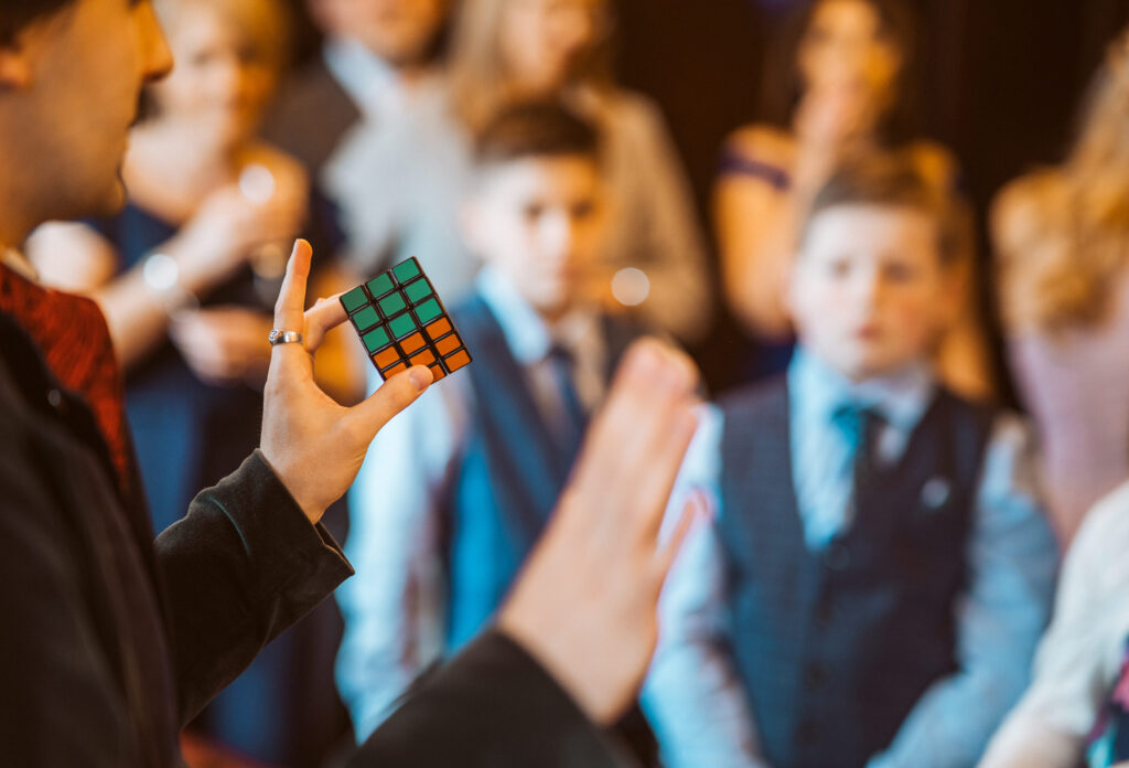 Close up of Jay Gatling doing magic with a Rubik's Cube, with wedding guests in the background.